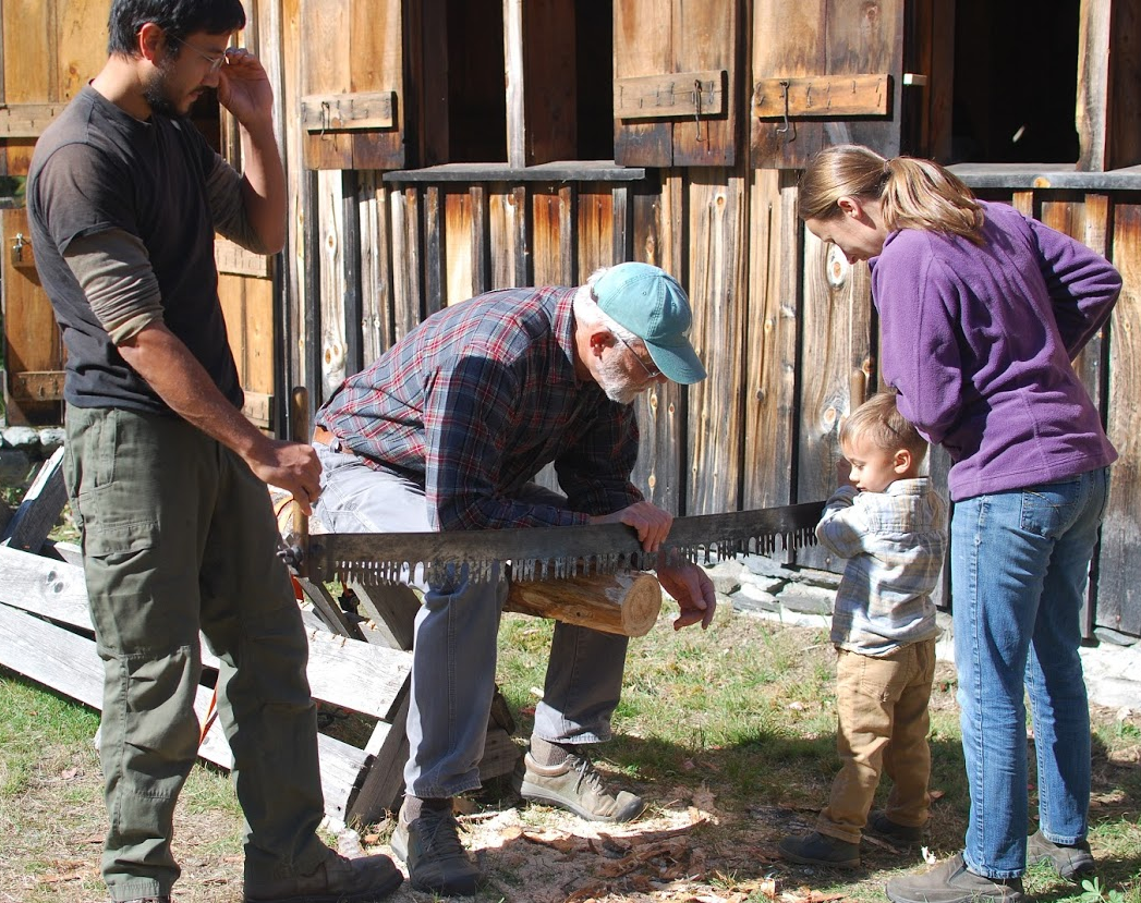 Parents and volunteer helping boy saw log.